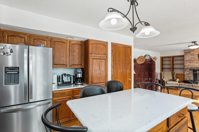 kitchen featuring a center island, hanging light fixtures, a textured ceiling, stainless steel fridge, and a fireplace