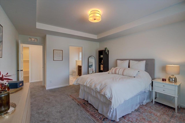 carpeted bedroom with connected bathroom and a tray ceiling