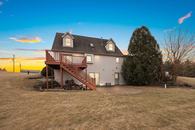 back house at dusk with a yard, a deck, and a patio