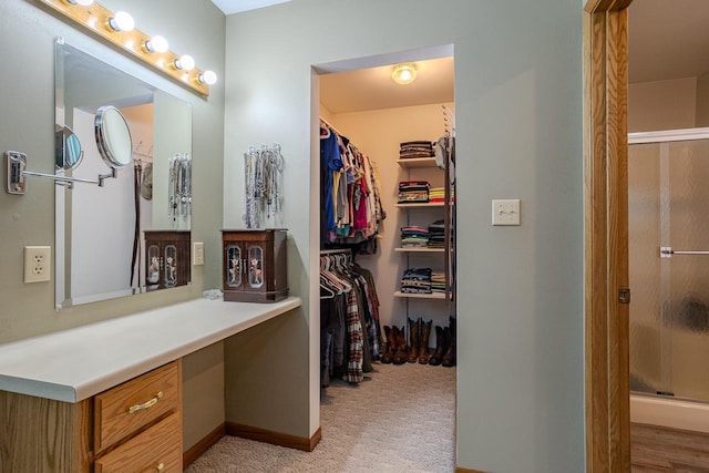 walk in closet with built in desk and light carpet