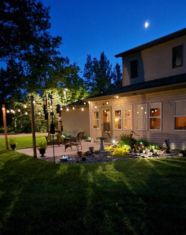 back house at twilight featuring a patio and a yard