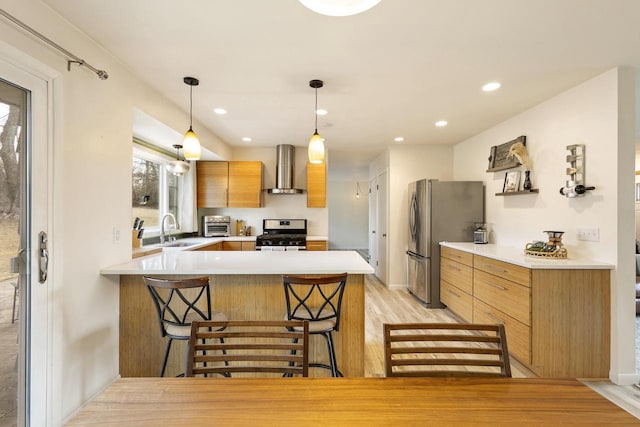 kitchen featuring sink, appliances with stainless steel finishes, a kitchen breakfast bar, kitchen peninsula, and wall chimney exhaust hood