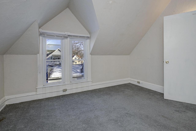 bonus room with dark colored carpet and lofted ceiling