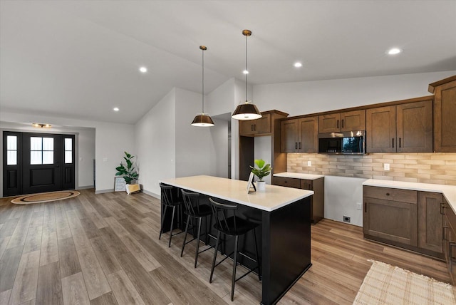 kitchen featuring a breakfast bar, a center island, hanging light fixtures, light hardwood / wood-style flooring, and backsplash