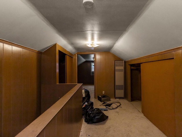 hall with lofted ceiling, light colored carpet, a textured ceiling, and wood walls