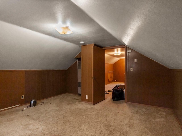 additional living space with vaulted ceiling, light colored carpet, and wood walls