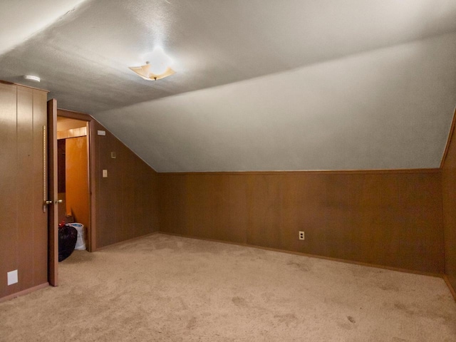 bonus room featuring lofted ceiling, wooden walls, and light carpet