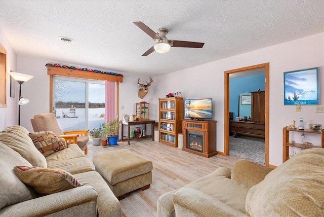 living room featuring ceiling fan, light hardwood / wood-style flooring, and a textured ceiling