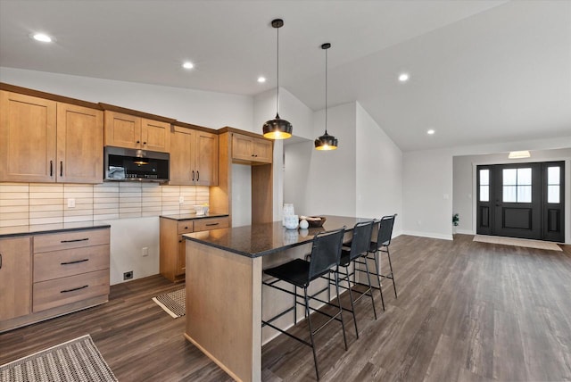 kitchen featuring a breakfast bar area, decorative light fixtures, a center island, dark hardwood / wood-style flooring, and backsplash