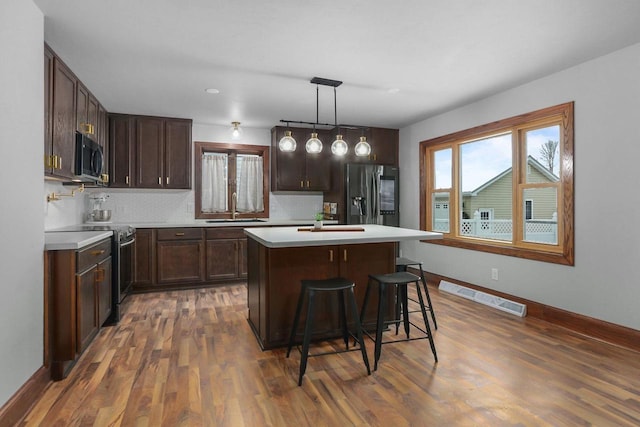 kitchen featuring sink, a breakfast bar area, appliances with stainless steel finishes, a kitchen island, and decorative light fixtures