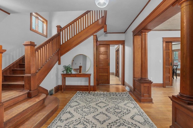 entryway with crown molding, decorative columns, and light wood-type flooring