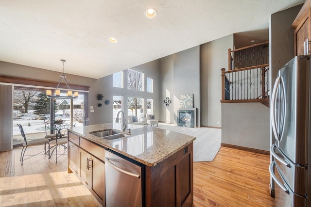 kitchen with sink, light stone counters, decorative light fixtures, appliances with stainless steel finishes, and an island with sink