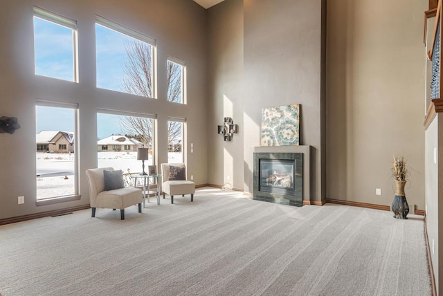 sitting room with light carpet, a tiled fireplace, a wealth of natural light, and a towering ceiling