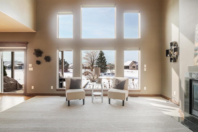 living area featuring light hardwood / wood-style flooring, plenty of natural light, a premium fireplace, and a high ceiling