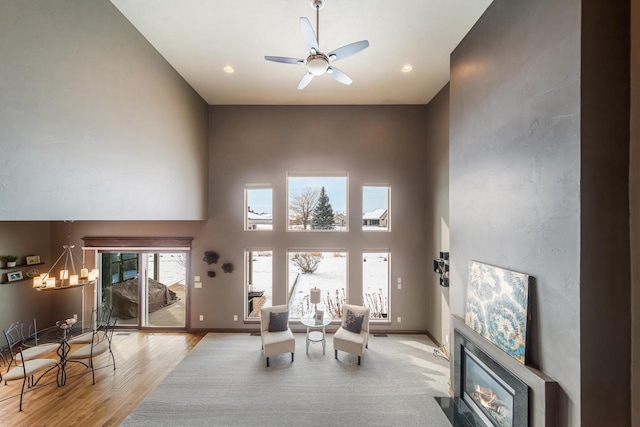 living room featuring ceiling fan with notable chandelier, light hardwood / wood-style flooring, and a high ceiling