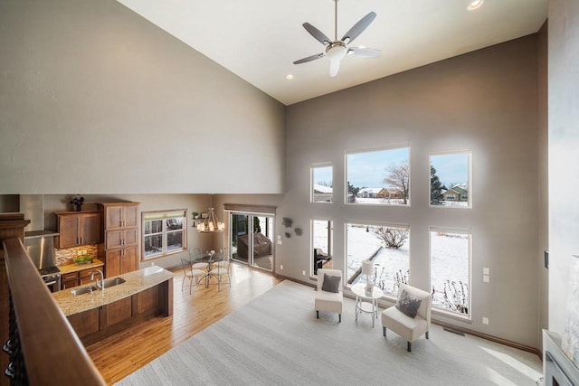 living room with sink, ceiling fan with notable chandelier, light wood-type flooring, and a high ceiling