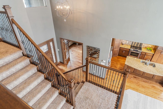 stairs with hardwood / wood-style floors, a notable chandelier, sink, and a high ceiling