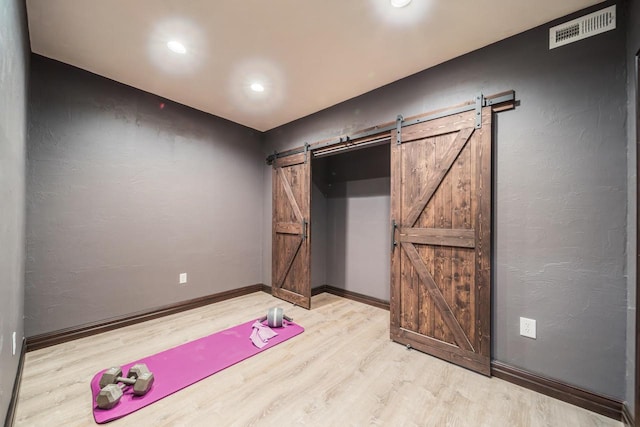 exercise room featuring a barn door and light hardwood / wood-style flooring