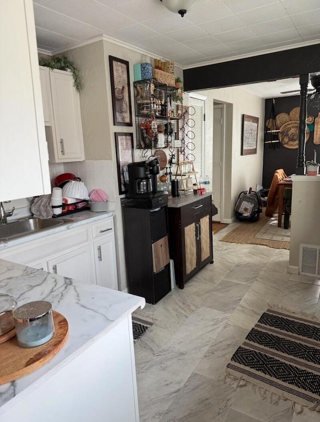 kitchen featuring white cabinetry, sink, ornamental molding, and light stone countertops