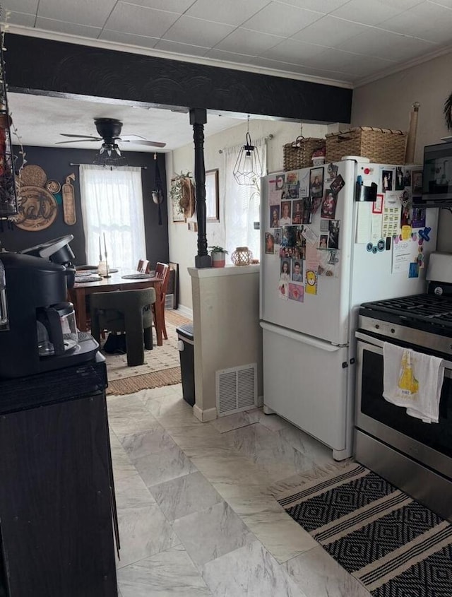 kitchen featuring stainless steel gas range oven, white fridge, ornamental molding, and ceiling fan