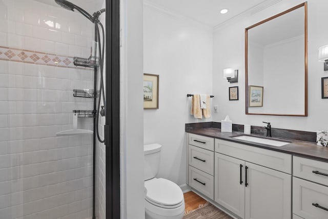 bathroom with tiled shower, toilet, crown molding, vanity, and hardwood / wood-style floors