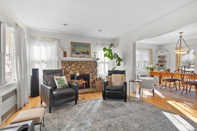 living area with radiator, a stone fireplace, plenty of natural light, and light hardwood / wood-style floors