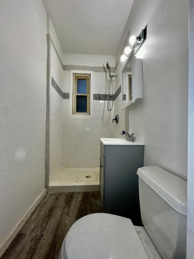 bathroom with vanity, wood-type flooring, toilet, and tiled shower