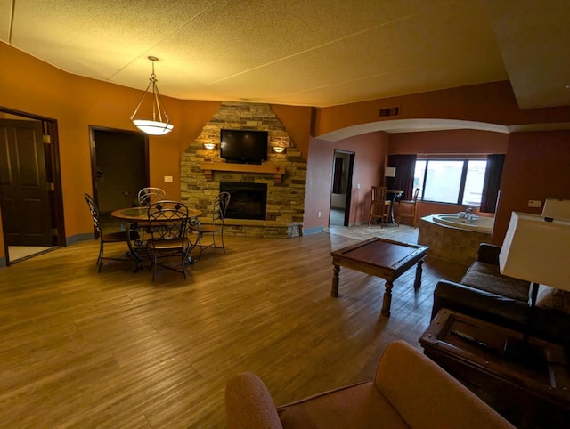 living room featuring a stone fireplace, hardwood / wood-style floors, and a textured ceiling