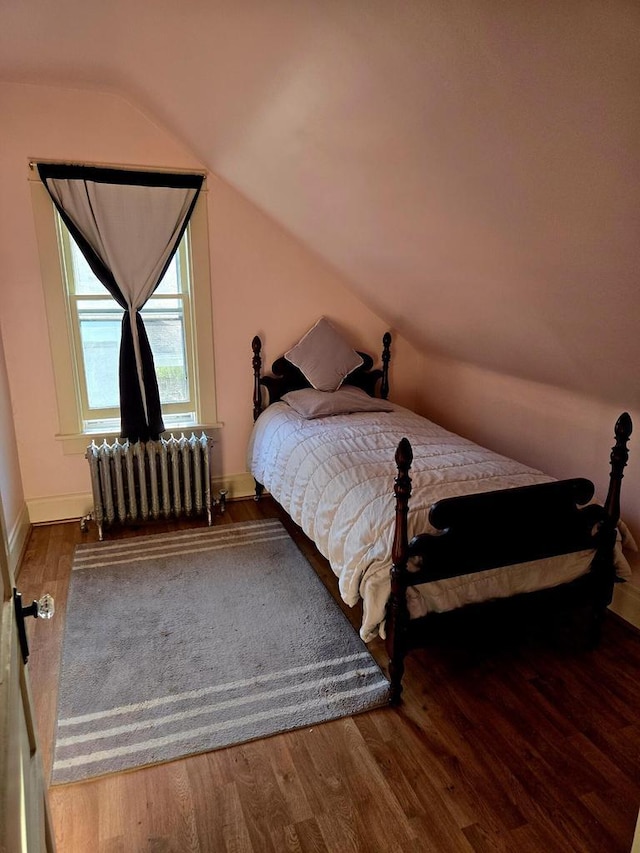 bedroom with vaulted ceiling, radiator, and hardwood / wood-style floors