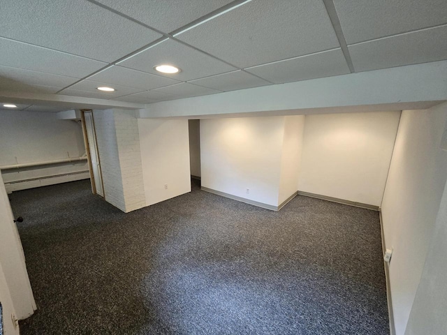 basement with dark colored carpet, a baseboard heating unit, and a paneled ceiling