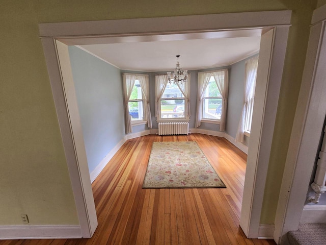 unfurnished dining area with crown molding, radiator, an inviting chandelier, and light hardwood / wood-style floors