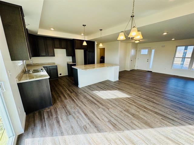 kitchen featuring dark wood-type flooring, sink, hanging light fixtures, a tray ceiling, and a kitchen island