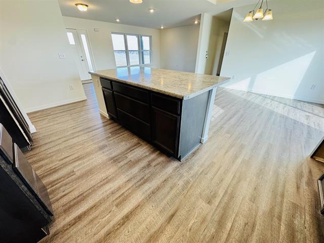 kitchen with pendant lighting, a center island, light stone counters, and light hardwood / wood-style flooring