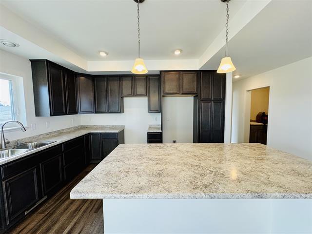 kitchen with pendant lighting, a center island, sink, and light stone countertops