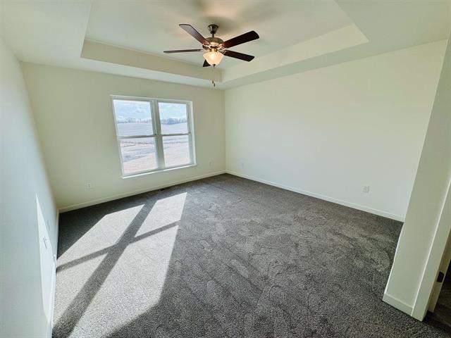 spare room featuring ceiling fan, a raised ceiling, and dark carpet