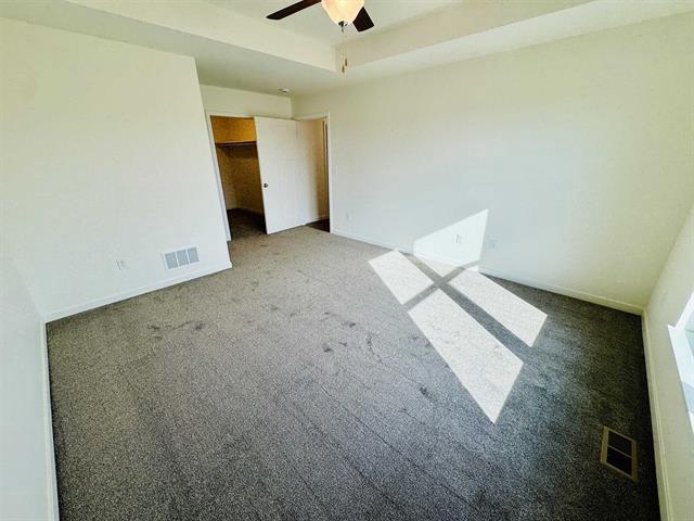 unfurnished room with ceiling fan, carpet flooring, and a tray ceiling