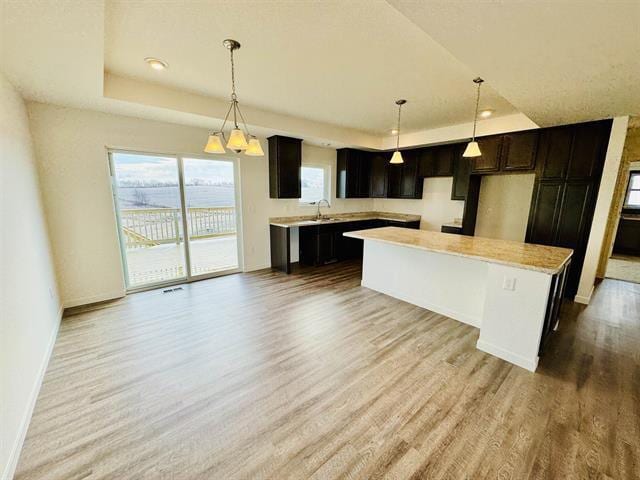 kitchen featuring a raised ceiling, a kitchen island, hanging light fixtures, and light wood-type flooring