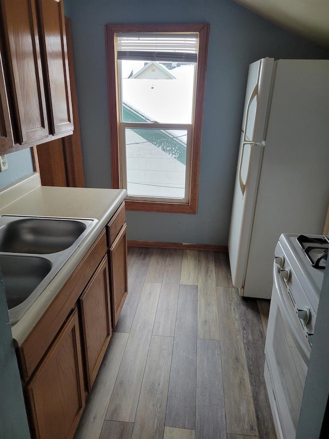 kitchen featuring sink, white appliances, light hardwood / wood-style flooring, and vaulted ceiling