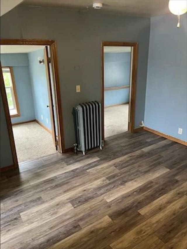 empty room with lofted ceiling, radiator, and dark hardwood / wood-style floors