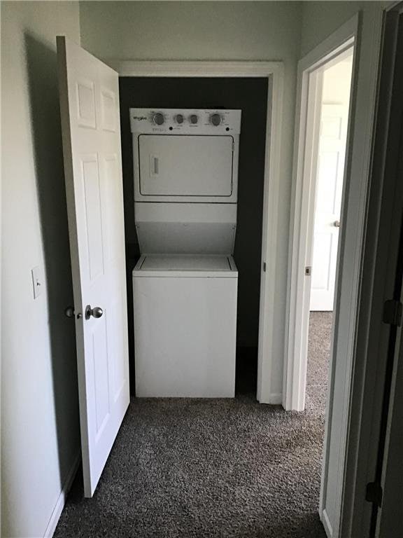 laundry room featuring stacked washer / drying machine and dark carpet