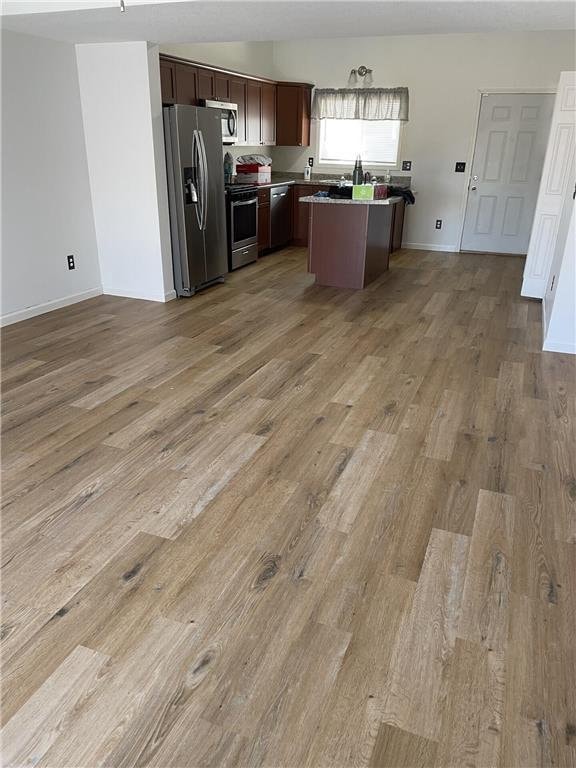 kitchen with dark brown cabinetry, stainless steel appliances, a kitchen island, and light hardwood / wood-style flooring