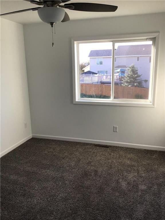 unfurnished room with dark carpet and ceiling fan