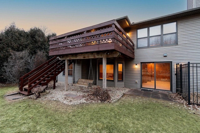 back house at dusk featuring a wooden deck and a lawn