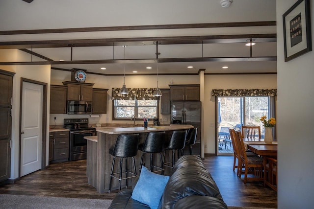 kitchen featuring dark hardwood / wood-style flooring, decorative light fixtures, an island with sink, and appliances with stainless steel finishes