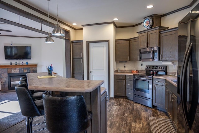 kitchen with appliances with stainless steel finishes, a fireplace, hanging light fixtures, ornamental molding, and dark wood-type flooring