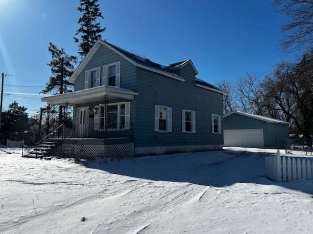 snow covered property with a garage, an outdoor structure, and covered porch