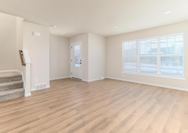 interior space with stairway, light wood-type flooring, visible vents, and baseboards