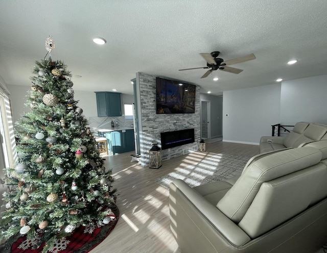 living room with hardwood / wood-style flooring, ceiling fan, a fireplace, and a textured ceiling