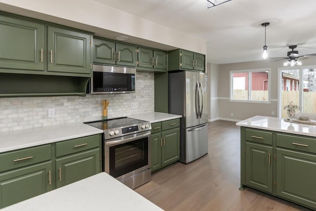 kitchen with appliances with stainless steel finishes, decorative backsplash, hanging light fixtures, green cabinets, and light hardwood / wood-style flooring