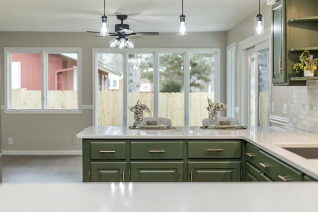 kitchen featuring ceiling fan, green cabinetry, hanging light fixtures, and backsplash